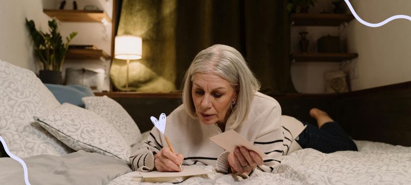 Woman in a striped top lying down on a bed writing in a journal